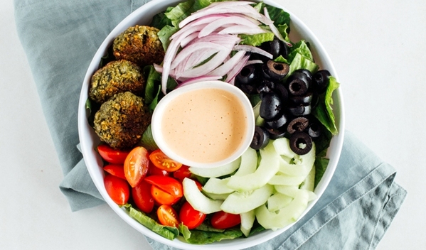 Ensalada Habibi con lechuga romana, tomate cherry, pepino, cebolla morada, aceituna negra, queso feta, falafel y aderezo lemon tahini.